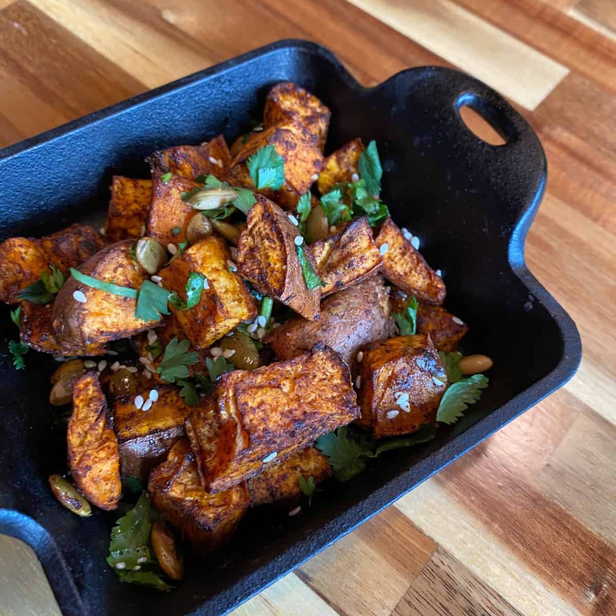 Seasoned Sweet Potatoes in a Cast Iron Dish on a Wood Table