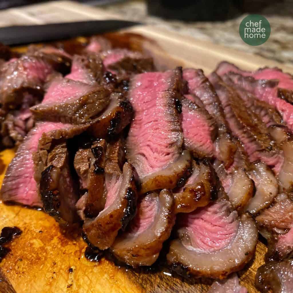 Sliced medium rare steak in a pile on cutting board
