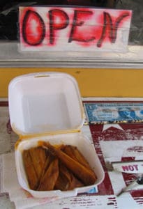 Styrofoam box with a half dozen red hot tamales with sauce in them. Open Sign with faded red ink.